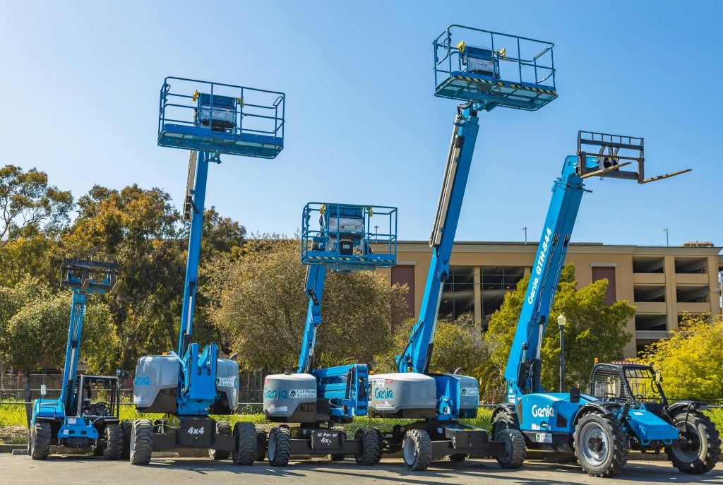 Outdoor scene with multiple blue aerial lifts and heavy machinery in a sunny industrial area.