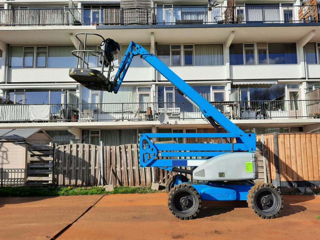 Blue construction lift in front of residential building under bright sunlight in Nederland.